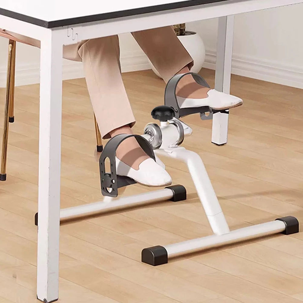 Person using a desk-based exercise pedal on a wooden floor.